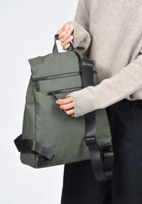 Mochila de tela verde y duradera con forma estructurada, dos cremalleras delanteras y correa de hombro ajustable. Asa superior reforzada.