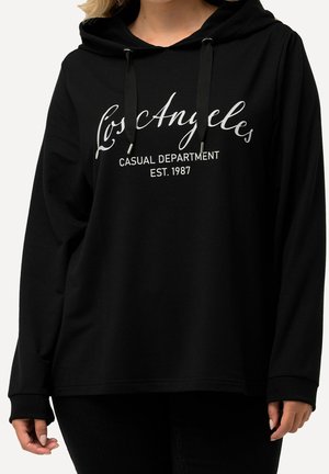 Sort hættetrøje med hvid tekst "Los Angeles Casual Department Est. 1987", båret af en person med lys hud og blondt hår.