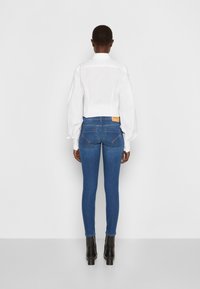 Vit topp med korta ärmar och puffärmar, kombinerad med blå skinny jeans. Jeansen har bakfickor och bruna sömmar. Svarta klackstövlar fulländar looken.