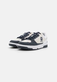 Sneaker con una toma beige e blu, caratterizzate da una combinazione di pelle testurizzata e suede, suola bianca e lacci blu. Logo visibile sul lato.