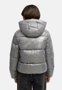 Chaqueta acolchada gris con capucha, textura brillante, costuras horizontales y puños elásticos. Presenta un diseño corto con un ajuste relajado.