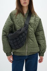 Veste bomber matelassée vert olive avec des poignets côtelés, assortie à un sac bandoulière hobo noir rembourré doté d'une sangle lisse.