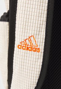 Bežna teksturirana platnena nahrbtnik z črnimi mrežastimi detajli. Ima oranžno logo Adidas, všito spredaj.