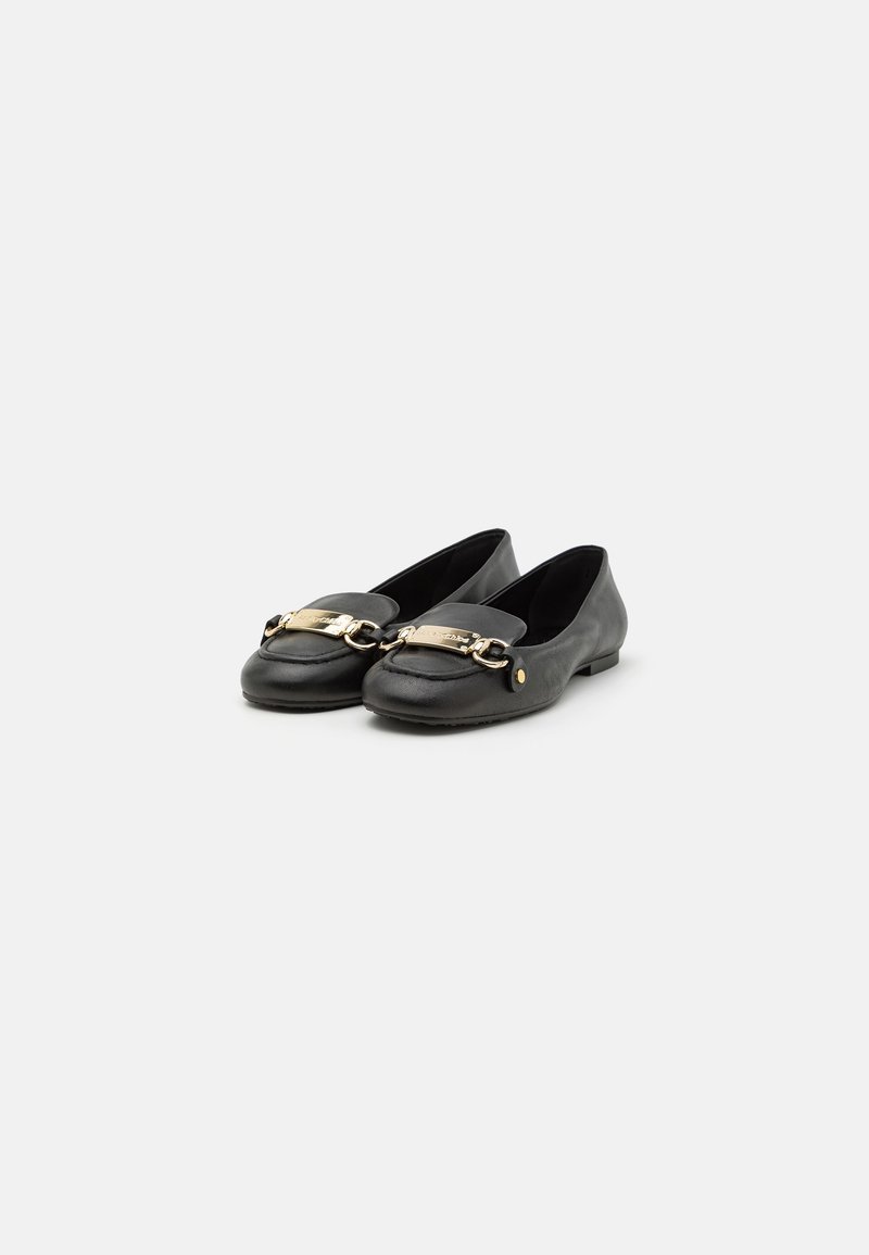 Mocassins en cuir noir avec chaîne dorée et détail métallique rectangulaire sur le dessus, semelle plate, placés en paire et légèrement inclinés vers la gauche sur fond blanc.