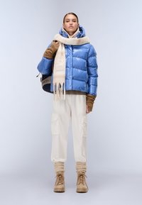 Lys blå oppustelig jakke, cremegul tørklæde, beige cargo bukser med lommer og brune støvler. Glat, skinnende tekstur; afslappet pasform; funktionelt design.