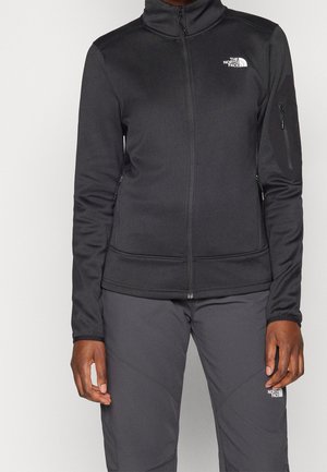 Osoba ubrana w czarną kurtkę na zamek i szare spodnie, na obu z logo The North Face na piersi i udzie.