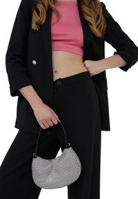 Borsa a tracolla argentata a forma curva con manico nero, abbinata a una giacca nera e pantaloni neri a vita alta, con un top rosa.