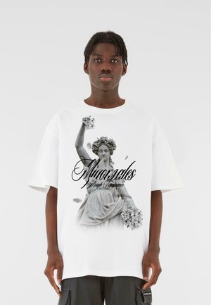Hvid oversized T-shirt med et sort-hvidt grafisk design af en statue, der holder blomster, med teksten "Minoracles Rough Renaissance" nedenunder.