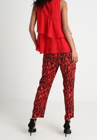 Haut sans manches rouge à plusieurs couches avec une texture légère, associé à un pantalon rouge orné d'un imprimé léopard noir, porté avec des chaussures à talons noires.