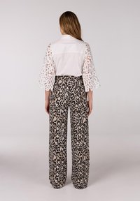 Witte blouse met kantmouwen en brede broek met luipaardprint. De blouse heeft een klassieke kraag; de broek heeft een gedurfde dierenprint.