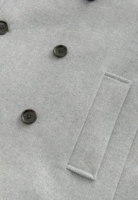 Grijze wolmix dubbele-breasted jas met zwarte knopen, visgraattextuur en een zijzakdetail.