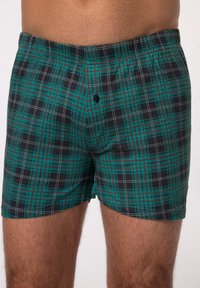 Boxerit lyhyet housut vihreä-mustassa ruudullisessa kuosisessa, jossa on valkoisia ja punaisia yksityiskohtia, pehmeää kangasta ja yksinkertainen nappikiinnitys edessä.