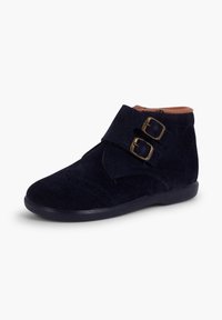 Botine din suede albastru marin până la gleznă, cu două catarame din alamă și o talpă netedă din cauciuc. Prezintă perforații decorative pe partea din față.