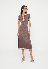 Hnedé šaty strednej dĺžky s výstrihom do „ V “ a krátkymi rukávmi, s jemnou textúrou a kontrastným golierom a lemovaním rukávov. Priehľadné, nadmerné slnečné okuliare.