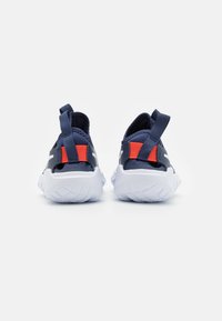 Chaussures de sport navy avec une surface texturée, semelle intermédiaire blanche et accents rouges et navy. Comprend des onglets de tirage pour un enfilage facile.