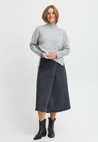 Hellgrauer, strukturierter Pullover mit hohem Kragen, kombiniert mit einem dunkelblauen Denim-Wickelrock und schwarzen Cowboy-Stiefeln. Lässiges, geschichtetes Outfit.