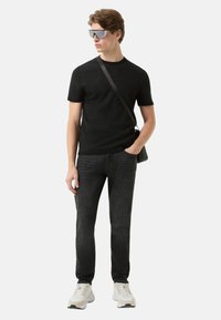 Sort t-shirt med korte ærmer, mørke jeans og lyse sneakers. Modellen bærer oversize grå solbriller og har en sort skuldertaske.