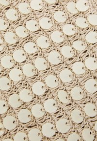 Bežová pletená látka se zaoblenými, plochými, světlými krémovými korálky rovnoměrně rozmístěnými a připevněnými skrze malé výřezy poblíž okrajů.