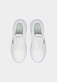 Ζευγάρι λευκών αθλητικών παπουτσιών Tommy Hilfiger με κορδόνια, διακριτικό λογότυπο στο πλάι και εσοχές με το εμπορικό σήμα, εμφάνιση από πάνω σε ουδέτερο φόντο.