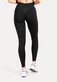 Leggings neri a vita alta con una texture liscia e un design aderente, abbinati a scarpe da ginnastica bianche con dettagli riflettenti.