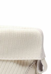 Textil color crema con textura acanalada en la parte superior, complementado por una base de cuero suave y costuras reforzadas. Diseño minimalista.
