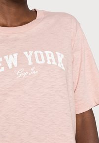 Lyserød bomulds t-shirt med rund halsudskæring og korte ærmer. "NEW YORK" er trykt i hvidt på brystet med fed skrift.