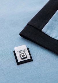 Štítkem označená modrá a černá textilní látka s nášivkou obsahující slovo "ambre" a čtvercový vzor. Textura vypadá hladká.