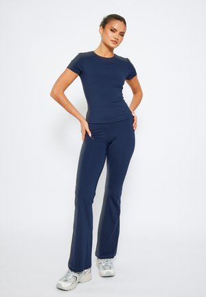 Navy blue activewear set features a fitted short-sleeve top and flared pants made of stretchy fabric, paired with silver athletic shoes.