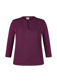 Lila Bluse mit langen Ärmeln, rundem Halsausschnitt, Knopfleiste und zwei aufgesetzten Taschen. Hergestellt aus weichem Stoff mit glatter Textur.