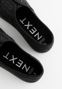 Juodai kanvosiniai slip-on tipo batai su raštuotu tekstūru, apvalia nosimi ir guminiais padais. Sidabriniai užrašai ant vidpadžio nurodo "NEXT" ir "FOREVER COMFORT."