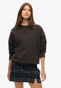 Ciemnoszara bluza z okrągłym dekoltem, luźnym krojem i oversize'owymi rękawami, zestawiona z granatową kratkowaną mini spódnicą z bocznym rozcięciem i pomarańczowymi akcentami.