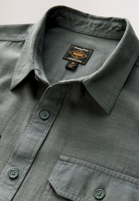 Gray button-up shirt with a textured fabric, point collar, and front pocket. Features matching gray buttons and a brand tag on the neckline.