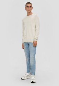 Hellbeige langärmliges Hemd, kombiniert mit hellblauen Jeans und weißen Sneakers. Einfaches Design, weicher Stoff und lässige Passform.