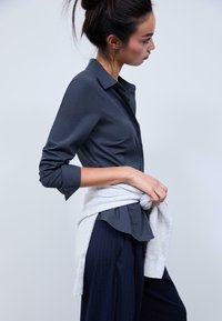 Dark gray collared shirt with long sleeves, paired with navy pinstripe pants. A light gray knit sweater tied at the waist adds texture.