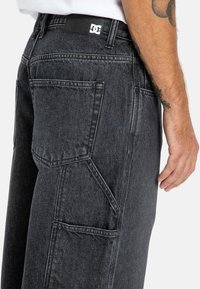 Czarne dżinsy o luźnym kroju, z dużymi bocznymi kieszeniami i widocznymi detalami przeszycia. Naszywka z logo na pasku.