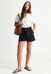 Black high-waisted shorts with a tied belt, paired with a white short-sleeve button-up shirt and brown flat sandals. Brown shoulder bag included.