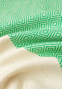 Tessuto intrecciato caratterizzato da un motivo geometrico verde di diamanti interconnessi e una sezione liscia di colore crema, con una finitura testurizzata.