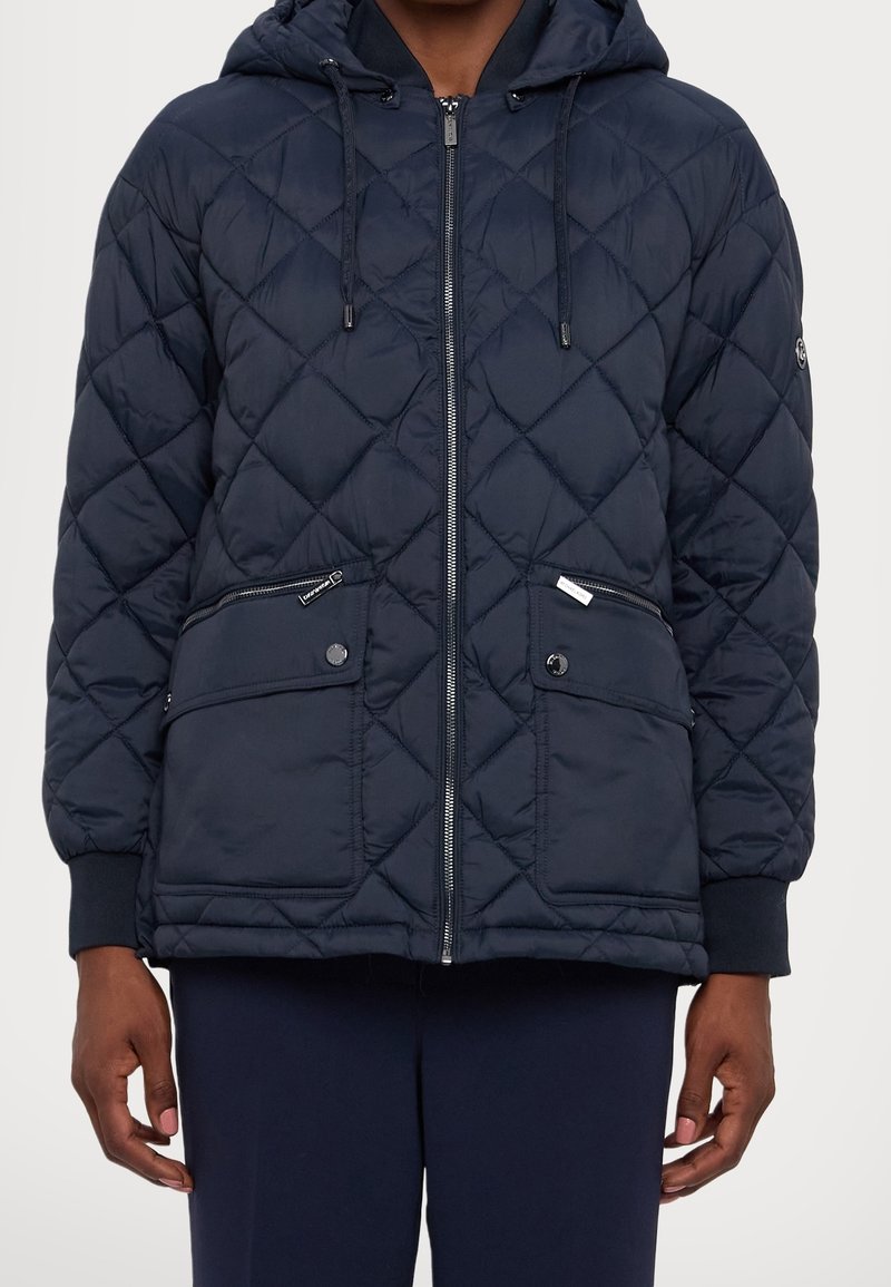 Marineblå quiltet dunjakke med hætte, lynlås, to forlommer, ribkant ved ærmerne og en glat, let tekstur.