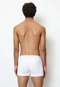 Boxer shorts bianchi in cotone con una fascia morbida, indossati da una persona vista da dietro, che mettono in mostra un design liscio e adattato.