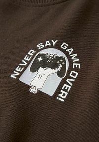 Bruin stof met een afbeelding van een hand die een zwarte gamecontroller vasthoudt. De tekst luidt "ZEG NOOIT GAME OVER!" in het wit.