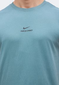 Μπλε μπλουζάκι Nike Pro, που δείχνει την περιοχή του στήθους με μαύρο λογότυπο Nike swoosh και κείμενο "NIKE PRO".