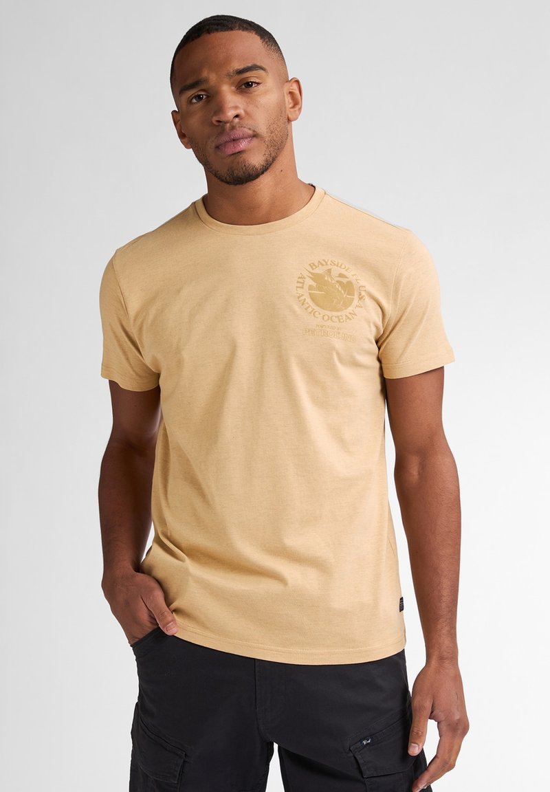 Beige katoenen t-shirt met korte mouwen en een ronde hals, met een cirkelvormig logodesign op de linkerkant van de borst. Soepele textuur.