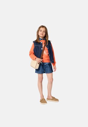 Veste en denim sur sweat-shirt orange avec impression blanche, short bleu à motifs, et sabots beige. Comprend un petit sac bandoulière beige.