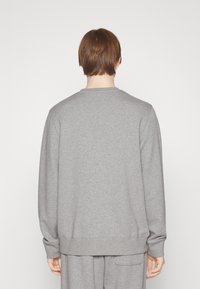 Grå tröja med rundad halsringning, långa ärmar och ribbade muddar. Har en slät textur och en avslappnad passform.