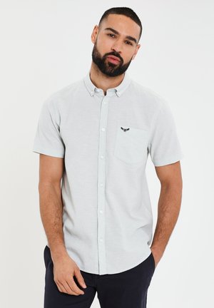 Lys grå kortærmet skjorte med knapper og brystlomme samt broderet design. Stoffet er en bomuldsblanding med en glat tekstur.