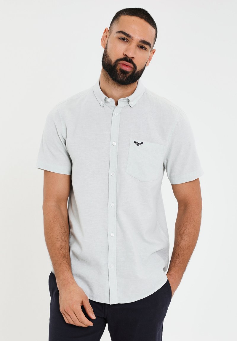 Camisa de manga corta de color gris claro, con botones y un bolsillo en el pecho, además de un diseño bordado. Tejido de mezcla de algodón con una textura suave.