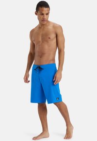 Niebieskie szorty kąpielowe z regulowanym paskiem w talii, wykonane z lekkiego materiału. Posiadają naszywkę z logo na dolnej części nogawki. Gładka tekstura.