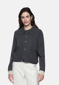 Dunkelgraue, kurz geschnittene Strickjacke mit großem Kragen, Frontknopfverschluss, zwei aufgesetzten Taschen und cremefarbenen, spitzenartig gemusterten Bündchen.