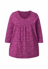 Tunique violette avec un motif floral, décolleté en V et manches trois-quarts, présentant un détail froncé au niveau de la poitrine pour plus de forme.