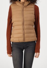 Veste matelassée marron avec fermeture éclair devant, manches en maille couleur rouille et capuche. Tissu texturé créant un effet superposé.